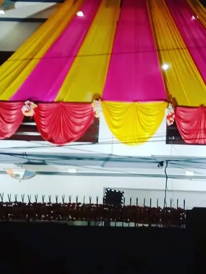 A tent-style canopy made of pink and yellow drapes covering the front of a house for a night event.