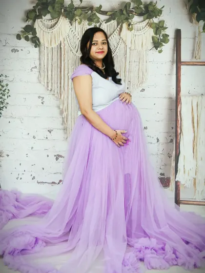 This lilac ruffled gown with a long train looks beautiful against a rustic, boho-inspired studio setup. The combination of the soft color and textured background creates a warm and inviting portrait.