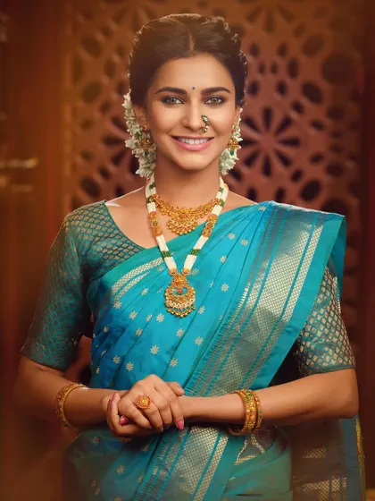 A smiling portrait highlighting a different set of traditional jewelry. The pearl and gold necklace adds a touch of softness to the vibrant blue saree, creating a look of pure elegance.