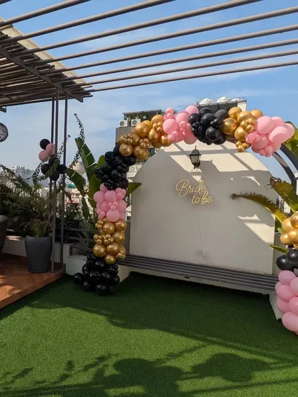 A wide shot of the black, pink, and gold balloon arch on a rooftop terrace, creating a stunning backdrop for a bachelorette party.