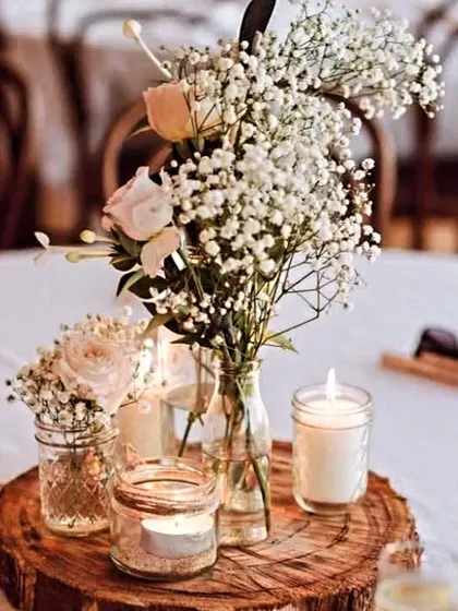The aesthetics of guest tables make the ambiance vibrant. This rustic centerpiece with baby's breath, candles, and a wooden base adds a charming and intimate touch to the dining experience.