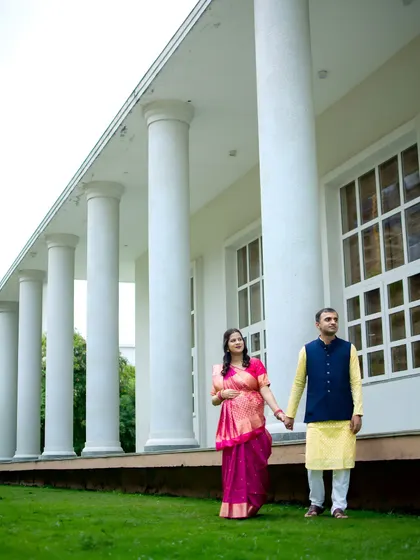 This grand architectural backdrop adds a touch of elegance to a traditional outdoor maternity shoot. The couple is dressed in a beautiful pink saree and a coordinated kurta set.