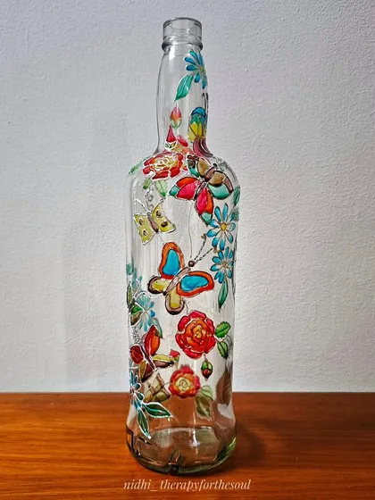 The butterfly and flower painted bottle shown indoors. Even without direct sunlight, the colors are bright and the design is a lovely decorative accent.