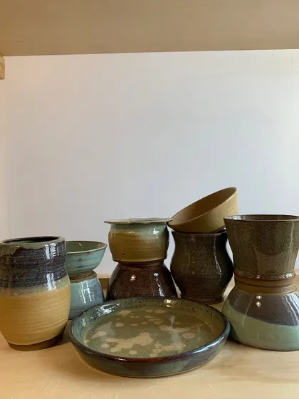 A stack of handmade bowls, plates, and vases in a variety of earthy glazes. Each piece is designed to be mixed and matched.