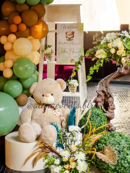 A welcome corner at a teddy bear-themed baby shower. A large teddy bear sits amongst balloons and floral arrangements, creating a warm and inviting entrance for guests.
