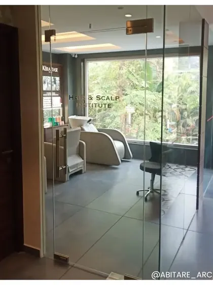 The entrance to the private Hair & Scalp Institute within the salon. The use of glass doors creates a sense of exclusivity while allowing natural light to flow through, with a view of the specialized treatment chairs inside.