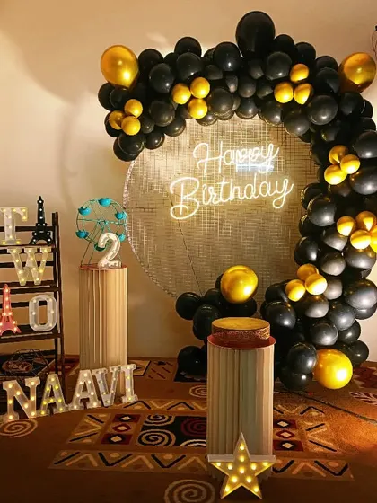A glamorous black and gold theme for Dhanaavi's second birthday. The sequin backdrop, neon sign, and metallic balloons create a sophisticated and celebratory atmosphere.