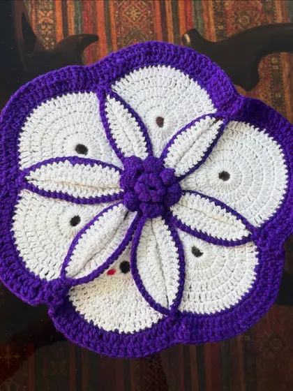 A top-down view of the purple and white floral crochet table mat, highlighting the layered petal effect in the center.