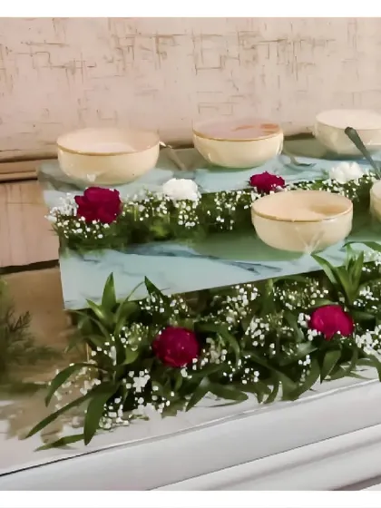 A dessert station featuring individual portions served in elegant bowls. The display is tiered and decorated with fresh red roses and baby's breath for a romantic touch.