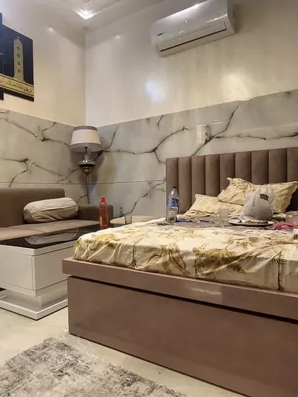 A view of a completed room that serves as both a bedroom and a sitting area. The space features a bed, a sofa, and Islamic wall art.
