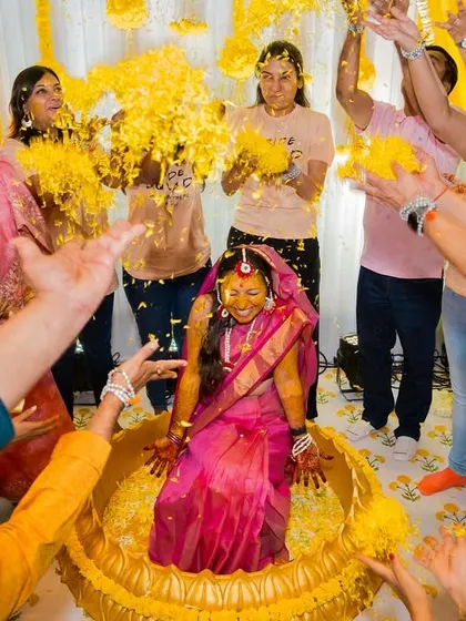 A wide-angle shot capturing the energy of the haldi, with everyone reaching in to shower the bride with flower petals.