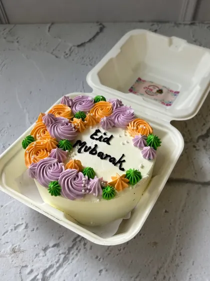 A vibrant Eid Mubarak bento cake decorated with purple and orange buttercream flowers. A colorful way to celebrate the occasion.