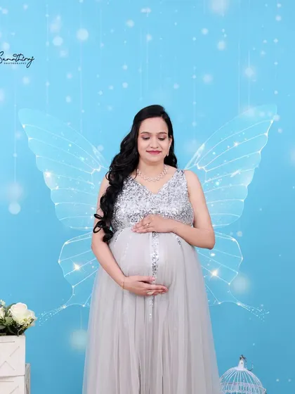 A magical portrait with a mother-to-be in a silver sequined gown, with ethereal butterfly wings edited in. The blue background and sparkling lights add to the fairytale feel.