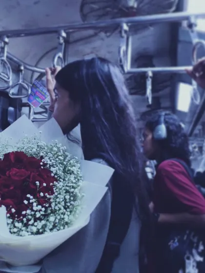 A quiet moment amidst the chaos of a Mumbai local train. A young woman holds a bouquet of red roses, lost in thought, showing how personal stories unfold even in the most public spaces.