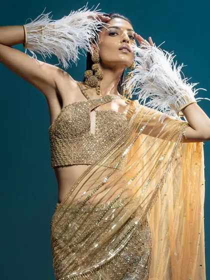 A glamorous gold sequin saree paired with dramatic white feather cuffs. This is an avant-garde look for a fashion-forward bride's cocktail or reception party.