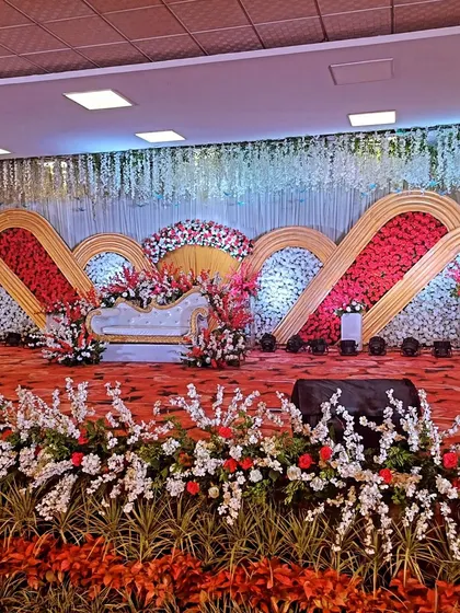 A full view of a grand reception stage with a red floral carpet and an elaborate, multi-arched floral backdrop.