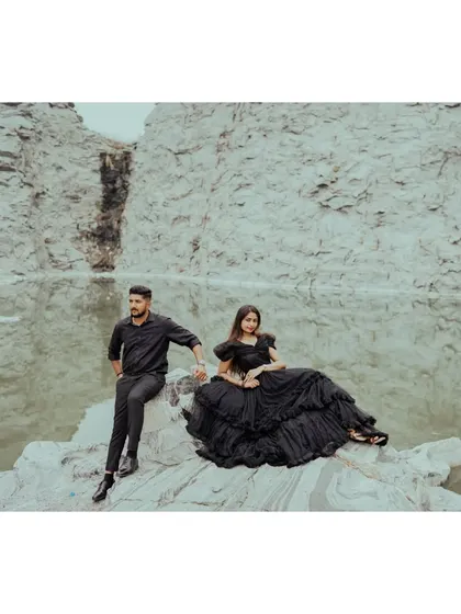 A couple sits on a rock by the water, dressed in black, creating a striking contrast with the natural landscape.