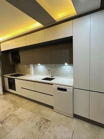 This wide shot shows the entire length of the galley kitchen, including the tall pantry unit at the end. The combination of recessed ceiling lights and under-cabinet LEDs ensures the kitchen is bright and functional at all hours.
