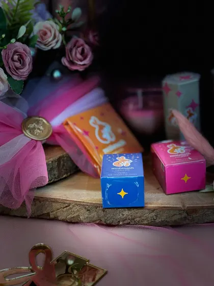 A close up of the Mishmash Naturals products, showing their cute packaging against a backdrop of pink flowers and a wood slice.