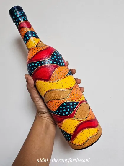 This bottle features a colorful, abstract patchwork design with stitched details. The warm reds and yellows are contrasted with patches of dotted blue.