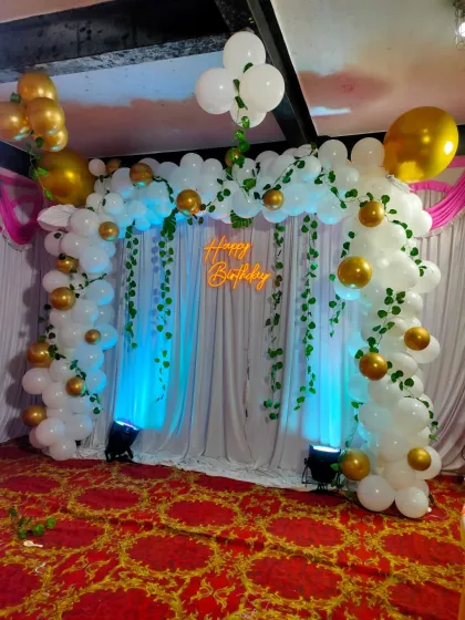 This wide shot shows the complete stage setup with the greenery-adorned balloon arch and lit backdrop.