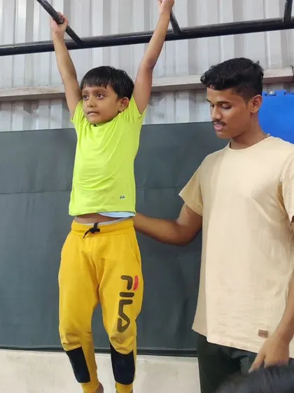 This image is a duplicate of 35, showing a coach providing support as a young boy practices hanging from the high bar. This hands-on guidance helps build confidence and ensures proper form.
