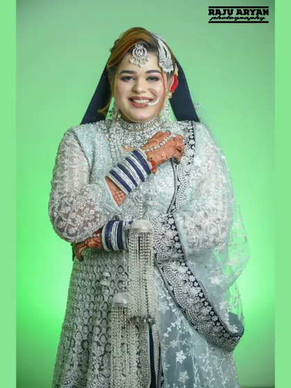 A bright, joyful portrait of a bride during her Nikah ceremony. Her beautiful smile is the centerpiece, captured against a clean, vibrant green background to make her silver and blue attire stand out.