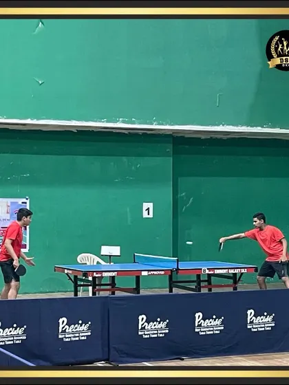 Two players in the middle of a competitive table tennis match. The setup includes professional tables and barriers for an uninterrupted game.
