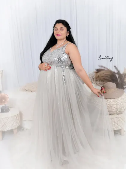 A serene portrait of a mother-to-be in a silver and white gown. The boho-chic setup with macrame and pampas grass creates a soft, dreamy, and stylish atmosphere.