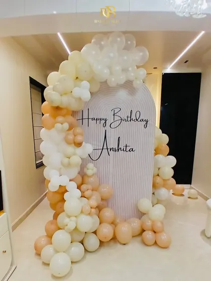 Soft and elegant decor for a personalized birthday celebration. This setup features a beautiful arch backdrop with the birthday person's name and a gentle cascade of pastel and cream-colored balloons.