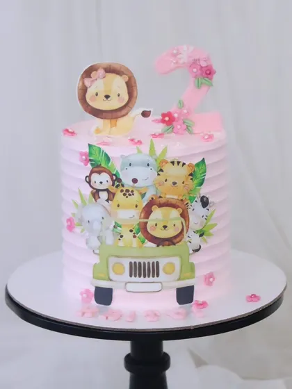 A pretty pink jungle safari cake for a little girl's second birthday. This design features a ribbed buttercream finish and is decorated with adorable printed safari animals in a jeep.