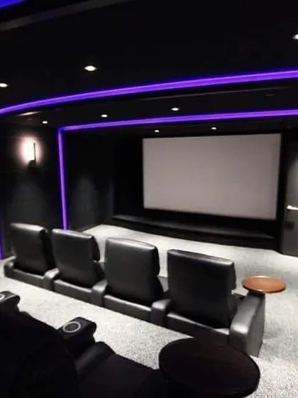 A sleek, minimalist home theater with black leather seating and cool purple ambient lighting. The clean design emphasizes the large screen and creates a distraction-free environment for the ultimate cinematic focus.
