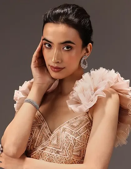 A close-up portrait showing a soft, peachy makeup palette. This look enhances the model's natural features and pairs beautifully with the ruffled sleeves of the gown.