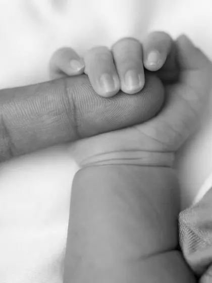 A close-up black and white photo of a newborn's hand tightly gripping an adult's finger, symbolizing trust and connection.