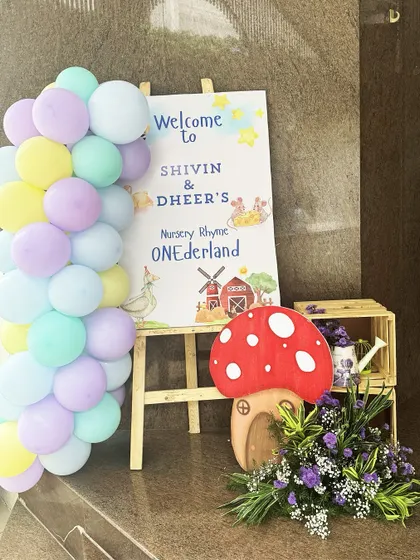 A personalized welcome sign on an easel, surrounded by pastel balloons and a giant mushroom prop, greeted guests at Shivin and Dheer's Nursery Rhyme ONEderland party.