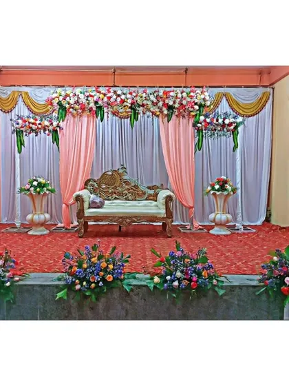 A classic stage decoration for a wedding reception or engagement. The combination of fresh flowers, elegant drapery, and traditional seating creates a timeless and beautiful backdrop for your special day.