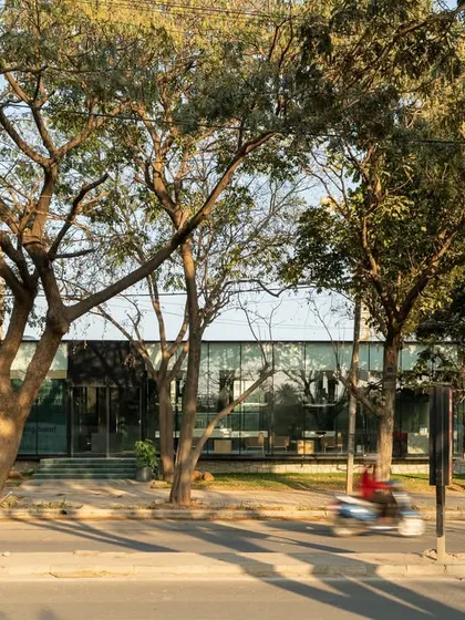 The VPG sales center seen from the street. The building is set back from the road, with a green buffer that creates a calm and welcoming approach. The transparent facade makes the interior feel like a part of the public realm.