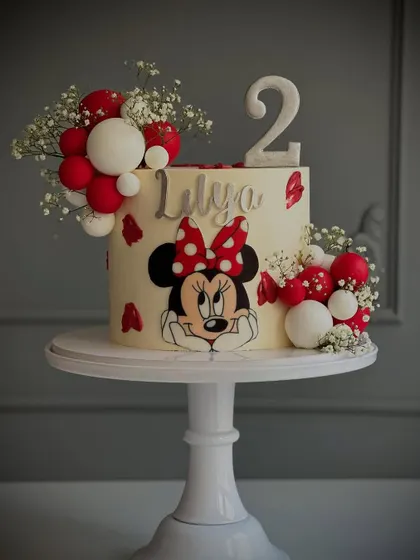 A sweet and simple Minnie Mouse cake, featuring a hand-painted character, polka dots, and festive red and white spheres.