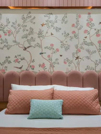 A close-up of the scalloped pink headboard set against a delicate floral and bird-patterned wallpaper. This combination creates a soft, romantic, and whimsical focal point in the daughter's bedroom.