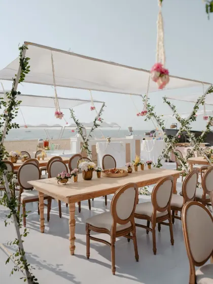 A chic and minimalist lunch setup by the beach in Goa. The white canopy, simple greenery, and elegant wooden furniture create a serene and sophisticated atmosphere.