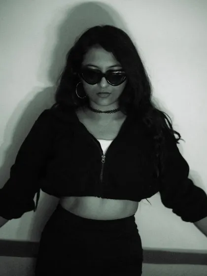 A full-body pose in a cropped hoodie and sunglasses. This monochrome image has a distinct urban and moody feel, showcasing a modern street-style look.
