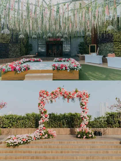 A beautiful outdoor setup featuring a stage with a hanging floral ceiling and a separate asymmetrical floral arch, both using a soft pink and red palette.