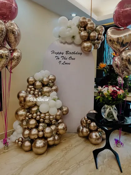 We create elegant and sophisticated backdrops perfect for birthdays or anniversaries. This setup features a stylish arch panel with a personal message, framed by a chic arrangement of chrome gold and white balloons, and complemented by floating heart-shaped foil balloons.