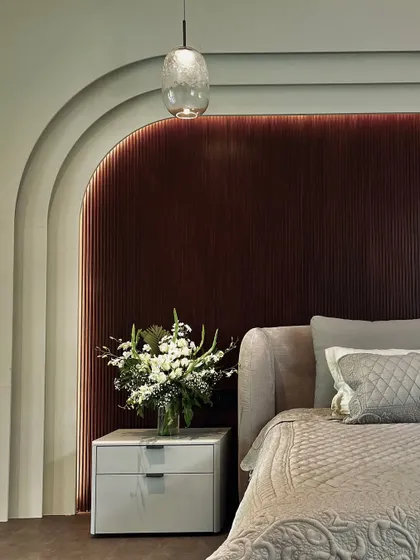 A close-up of the bedroom sanctuary, focusing on the bedside details. The arched, fluted headboard is complemented by a sleek marble-topped nightstand and a bouquet of fresh flowers, creating a composition of refined elegance.