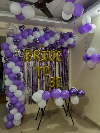 A simple and festive 'Bride to be' decoration for an intimate home celebration. This setup uses a purple and white balloon arch over a shimmery purple foil curtain.