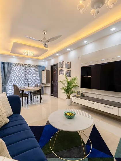 A wide view of the living room, showcasing a bold blue sofa, a geometric rug, and a large, minimalist TV unit.