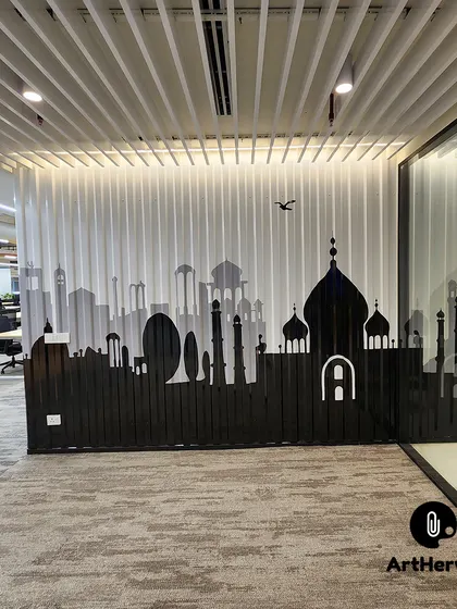 This view shows the Indian monument silhouette next to the office's glass-walled meeting rooms. The contrast between the black art and the open workspace is striking.