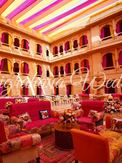 A stunning Mehendi setup inside a heritage palace in Jaisalmer, with vibrant pink and orange decor complementing the sandstone architecture.