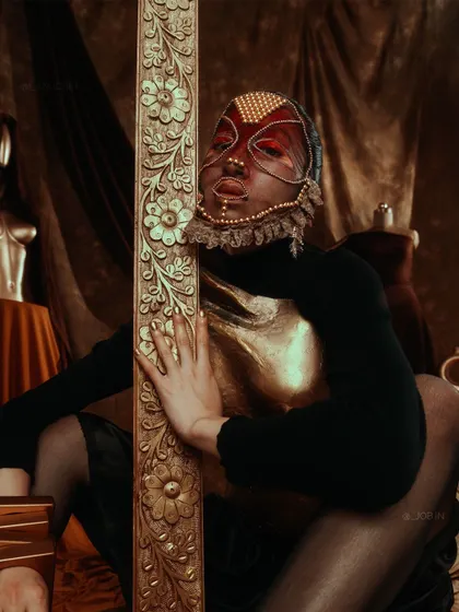 From the 'ASTRID' series, this shot highlights the intricate, custom-designed mask and golden breastplate. The styling is meant to feel regal and otherworldly, set against a rich, textured backdrop.