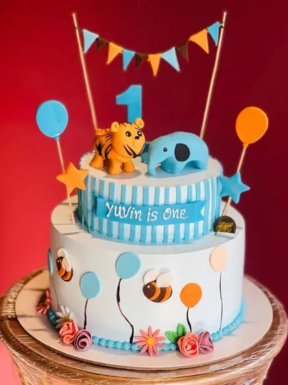 A cheerful two-tier cake for Yuvin's first birthday. This design includes cute animal toppers, balloons, and a festive banner, perfect for a little one's milestone celebration.